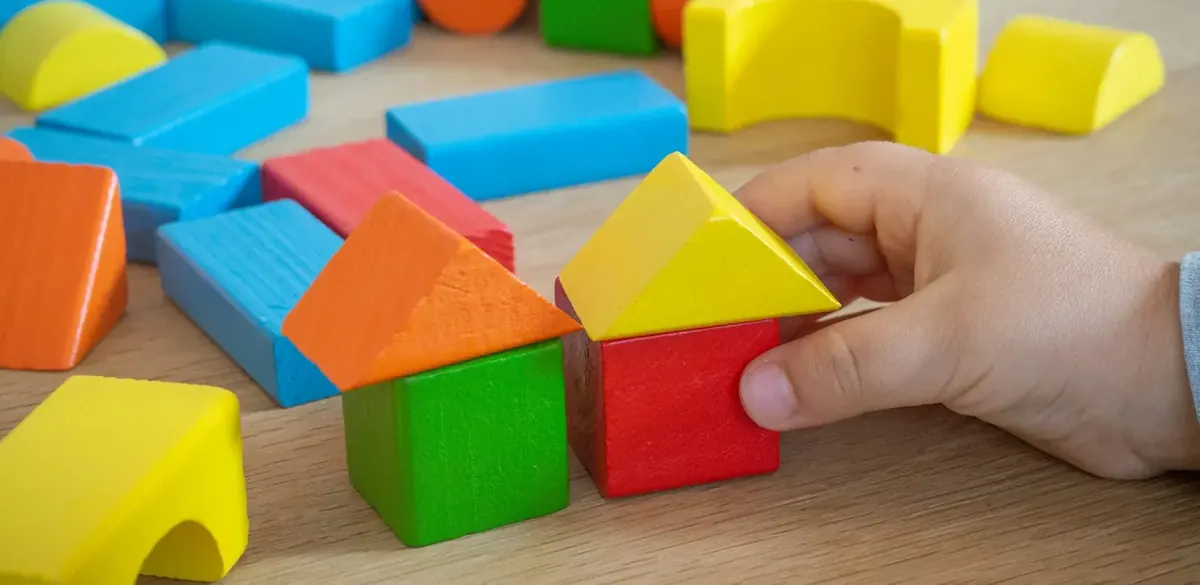A hand playing with colorful wooden blocks on a table.